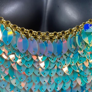 Détail macro de paillettes bleues irisées et chaîne dorée sur un haut dos nu sexy