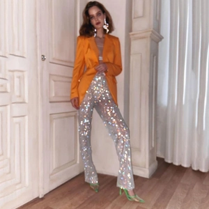 Dettaglio dei pantaloni a rete con paillettes argento e blazer in raso arancione vivace