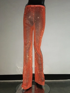 Dettaglio dei pantaloni a gamba larga in rete arancione a vita alta con strass scintillanti