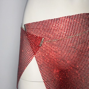 Détail d'une mini-jupe en maille à strass rouges brillants avec fente latérale et chaîne dorée