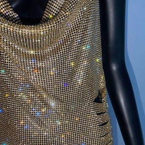 Dettaglio del tessuto a rete con strass dorati e anelli metallici su un abito da festa
