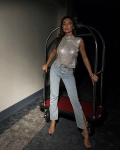 Detail of sparkly silver metal mesh sleeveless top and high slit denim jeans on a model