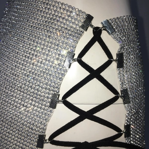 Détail du tissu en maille strass argentée avec lacets élastiques noirs et attaches en métal