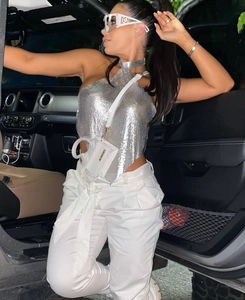 Detail of silver metallic mesh halter top paired with white high-waisted pants in a car
