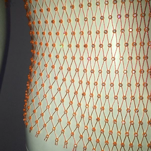 Detailed close-up of orange mesh top with sparkling rhinestones on fabric intersections