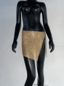 Détail d'une mini-jupe dorée en strass avec maille métallique et finitions à franges