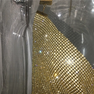 Détail d'une robe en maille métallique dorée scintillante avec strass brillants et boucle