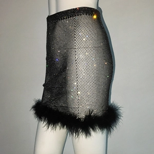 Détail d'une jupe en maille noire avec strass brillants et bordure en plumes