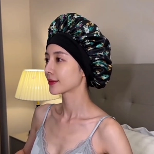 Detail of floral satin sleep bonnet with wide elastic band worn by a model in a bedroom