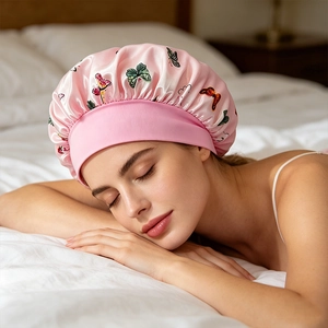 Pink satin sleeping cap with butterfly print and wide elastic band on a white pillow