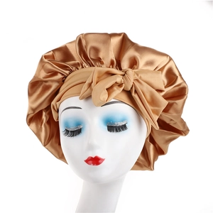 Detailed close-up of champagne satin sleep bonnet with bow tie on a mannequin head