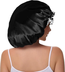 Detail of black satin hair bonnet featuring large printed bow and silky texture