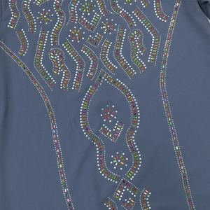 Détail macro de strass colorés sur robe en mousseline bleue montrant l'artisanat