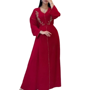 Dettaglio del ricamo floreale dorato e perle bianche su un caftano rosso con scollo a V