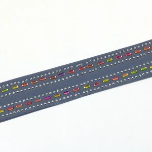 Détail des strass colorés et des perles de cristal sur une ceinture grise en mousseline