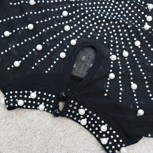Détail macro d'une robe en maille noire avec col goutte, perles et strass