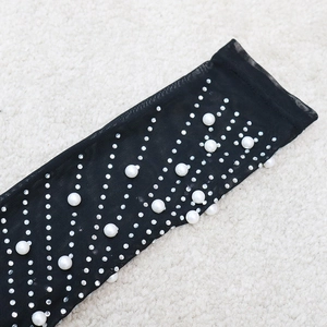 Détail de manches en maille noire transparente ornées de strass argentés et de perles