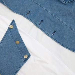 Detail of blue denim dress with embossed metal button and contrast stitching texture