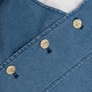 Detail of blue denim dress featuring three textured gold metal buttons on the front placket