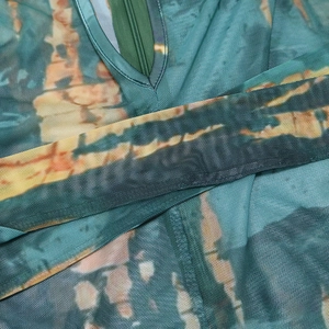 Close-up of sheer mesh jumpsuit with green tie-dye print and V-neck zipper detail