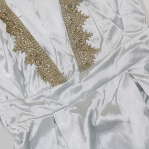 Detail of light blue satin dress featuring gold lace embroidery and pleated waist design