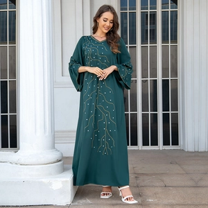 Détail de robe kaftan ample vert foncé avec motifs de feuilles dorées et pois blancs