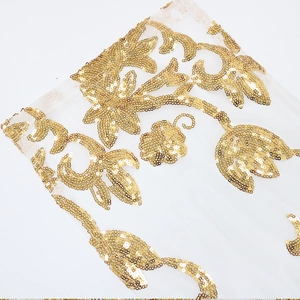 Detailed close-up of golden sequin floral embroidery on white mesh evening dress fabric
