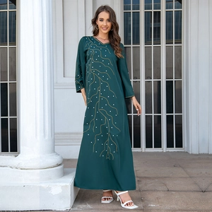 Détail d'une robe Abaya ample vert foncé avec broderie de perles dorées et blanches