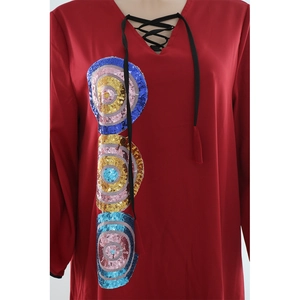 Detail of red V-neck dress featuring lace-up ties and three sequin embroidered badges