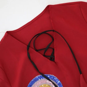 Detail of red V-neck dress featuring black lace-up ties and colorful sequin embroidery