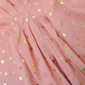 Dettaglio del tessuto in chiffon rosa con pois dorati e morbida trama plissettata