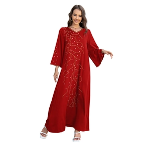 Détail de robe longue rouge foncé ample avec motifs de branches dorées et strass brillants
