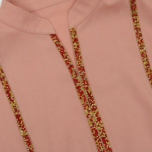 Détail d'une Jalabiya vieux rose avec garniture en paillettes rouges et dorées sur le col V