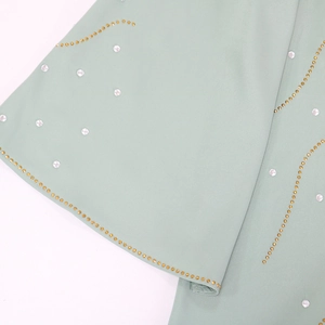 Détail d'une robe vert clair avec des strass et des motifs de vagues à clous dorés
