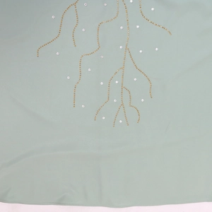 Vue détaillée du tissu vert menthe avec broderie de perles dorées et strass argentés