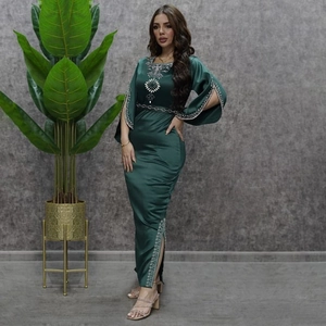 Abito da sera verde scuro con strass, maniche a campana e spacco laterale su sfondo grigio