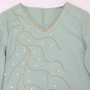 Détail du col en V sur robe longue vert clair avec strass dorés et blancs élégants et brillants