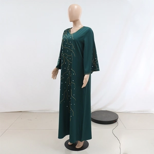 Détail d'une abaya vert foncé avec broderies dorées ondulées et perles blanches