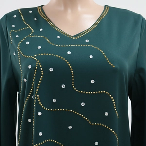 Détail de robe vert foncé à col en V avec rivets dorés et motifs de strass scintillants
