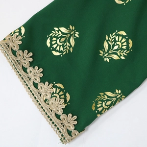 Close-up of ethnic dress showing green fabric with gold foil leaves and lace trim