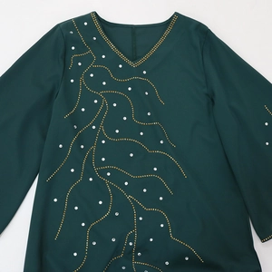 Détail de l'encolure avec des perles dorées et motifs en strass sur la robe longue verte