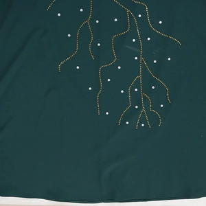 Détail du tissu vert foncé avec des motifs de vagues dorées et des strass étincelants