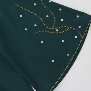 Détail d'une robe vert foncé montrant des strass étincelants et des motifs ethniques fins