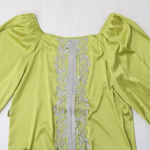 Detailed close-up of lime green satin dress with puff sleeves and silver lace embroidery
