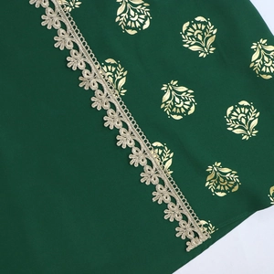 Detail of dark green fabric with gold floral stamping and white water-soluble lace trim