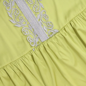 Macro shot of green kaftan dress featuring white lace embroidery and delicate pleats