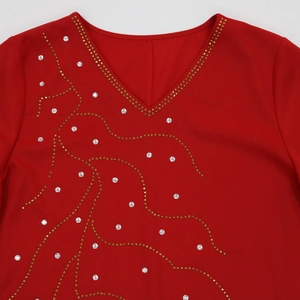 Détail de robe rouge à col en V avec des clous dorés et des motifs de strass scintillants