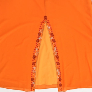 Détail macro d'une robe en mousseline orange avec broderie de strass et paillettes au col V