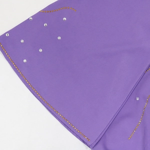 Détail du tissu violet avec des ornements ondulés en strass dorés et argentés