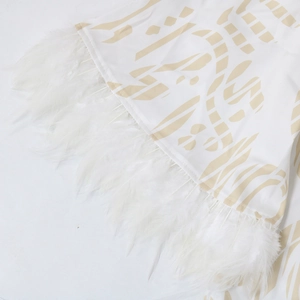 Nahaufnahme des Kaftankleid-Saums mit goldenem Print und luxuriösem weißen Federbesatz